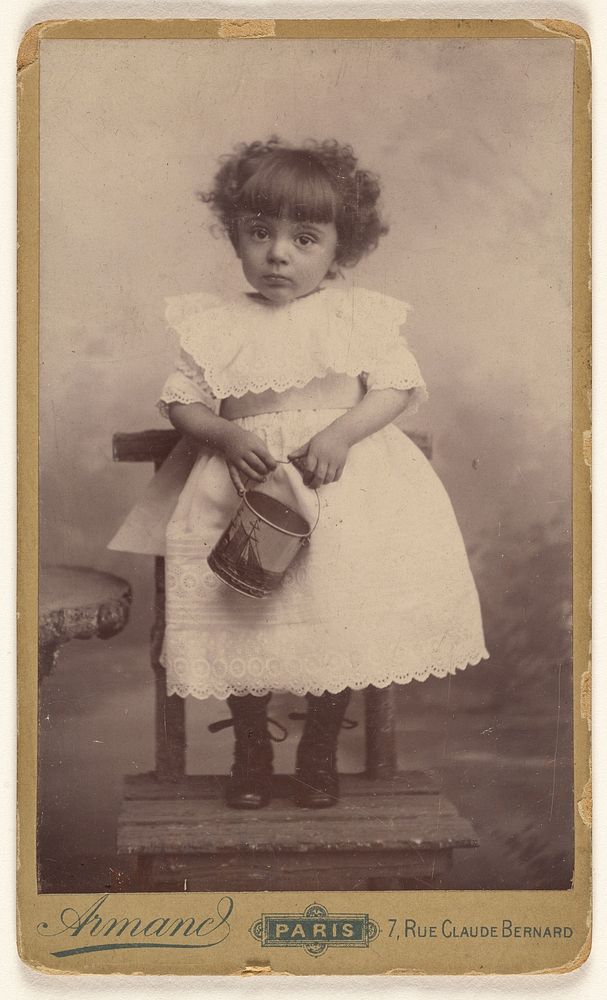 Unidentified little girl standing in a chair, holding a pail with a ship on it by Armand