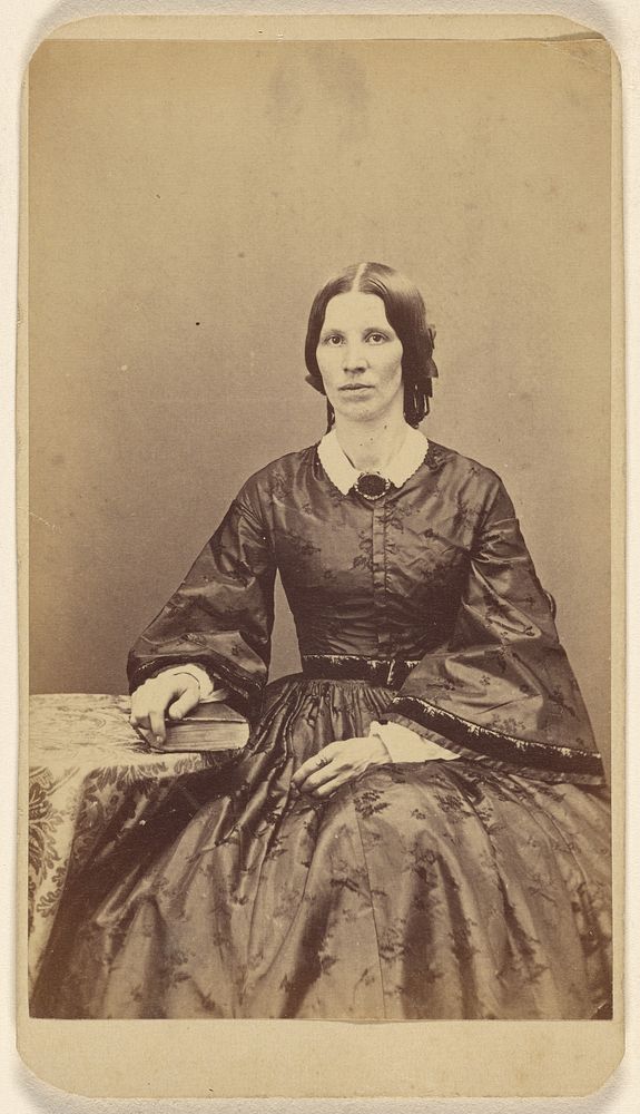 Unidentified woman seated, resting a hand on a book on a table by L T Sparhawk