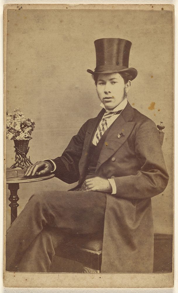 Unidentified young man wearing a top hat, seated by T Lake