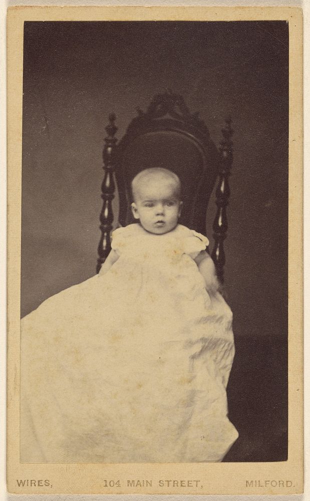 Unidentified baby wearing a long gown, seated in a high backed chair by W M Wires