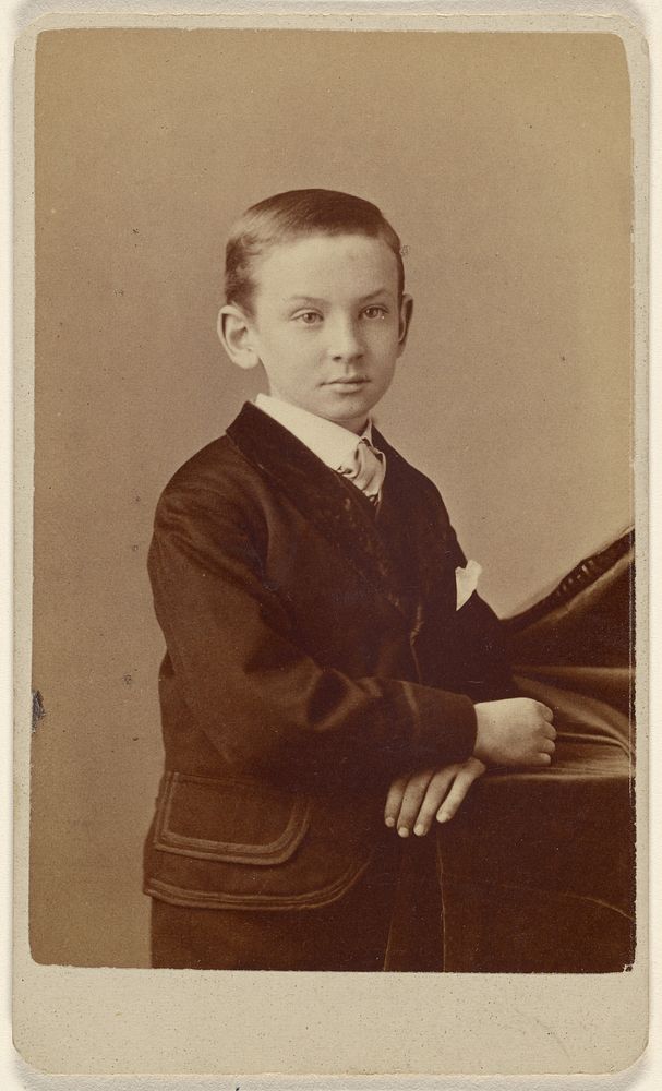 Unidentified little boy standing, leaning on cloth-covered table by Alva Pearsall