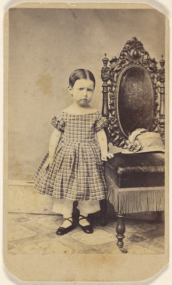 Unidentified little girl standing near an ornate chair
