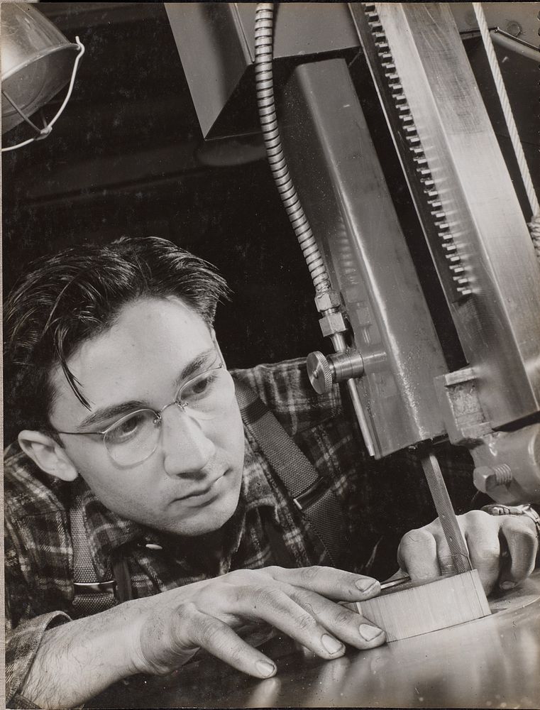 Man wearing glasses works intently with an industrial file by Arnold Eagle