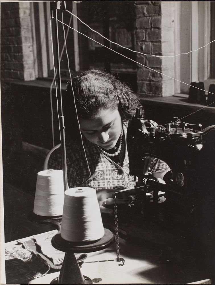 Woman uses a sewing machine threaded from two spools of white thread by Arnold Eagle