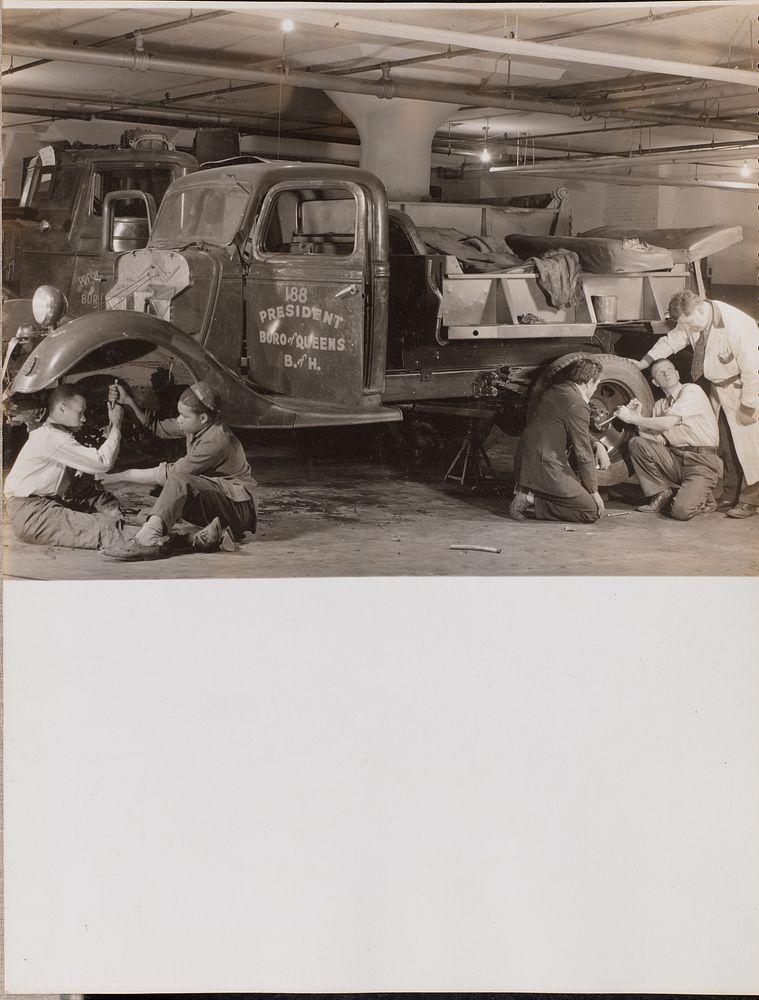 Two groups of young men work on the wheels of a truck by Arnold Eagle