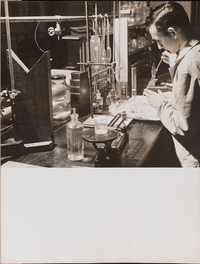 Man in a lab uses both hands to place a large pipette into a beaker by Arnold Eagle