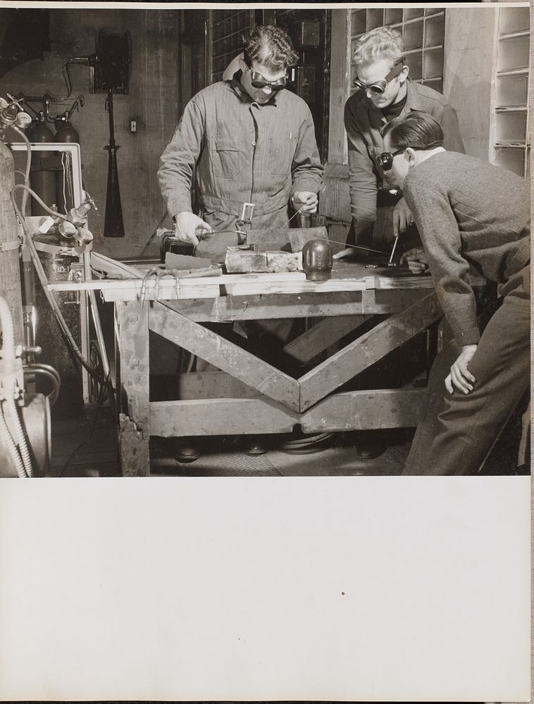 Three men wearing goggles weld a piece of metal on a table by Arnold Eagle