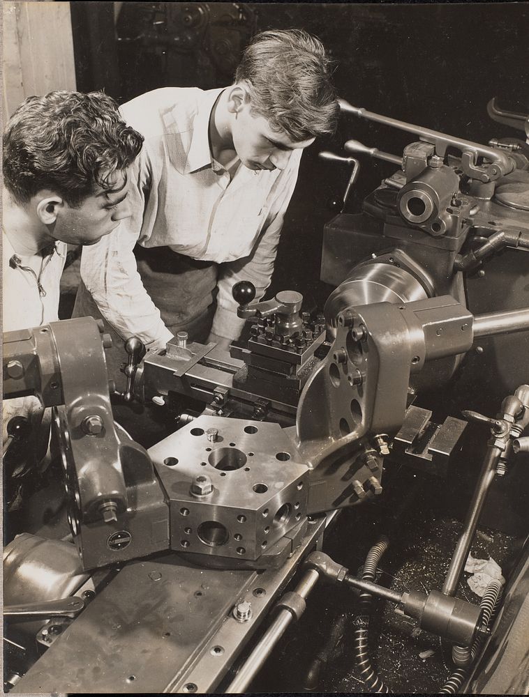 Two young men stand over a piece of machinery by Arnold Eagle
