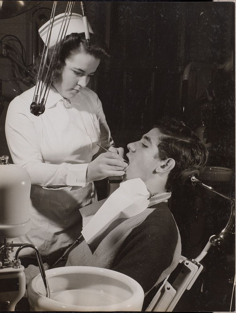 Dental hygienist inspects a patient's mouth by Arnold Eagle