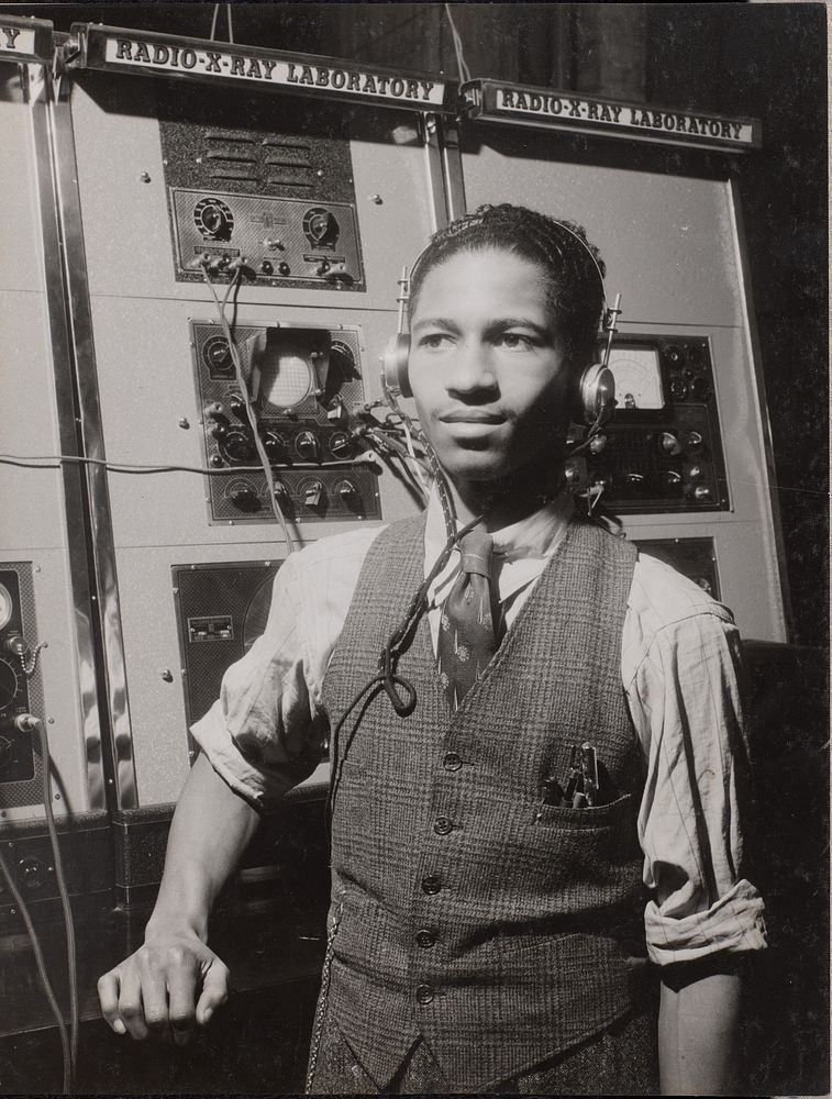 Man wearing headphones stands in front of a large machine by Arnold Eagle