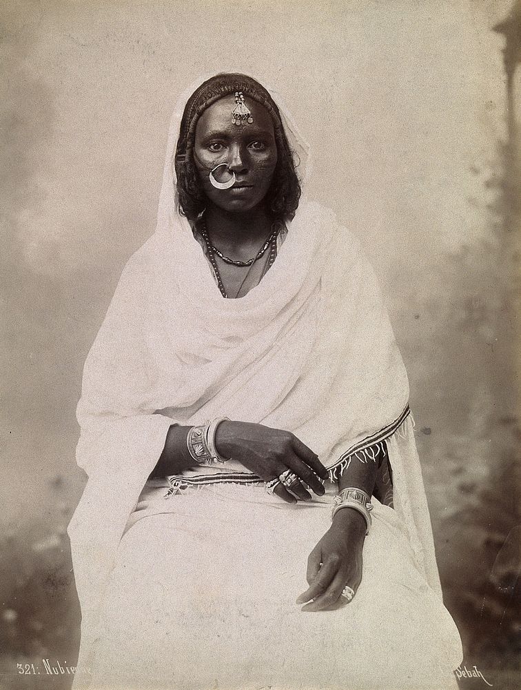 A Nubian woman, seated, with a large nose ring in her right nostril. Photograph by Sébah, 18--.