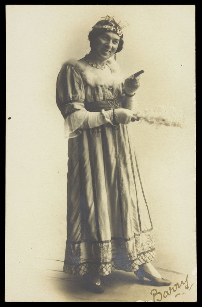 A man in drag, holding a feather, performing in the play 'A country girl'. Photographic postcard, 1920.
