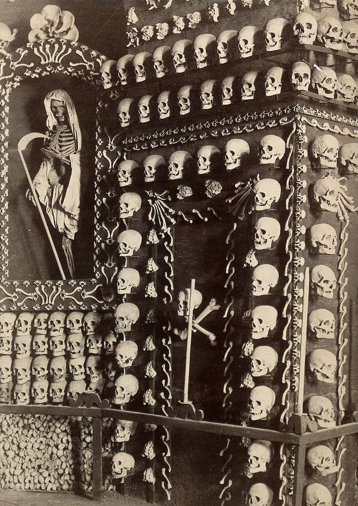Skulls and skeletons of friars arranged columns around the walls of a chapel. Photograph.