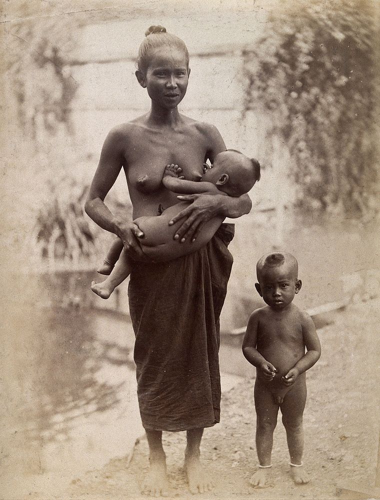 Thailand: a woman breastfeeding a child, standing, with a second child beside her. Photograph, 1880/1900.