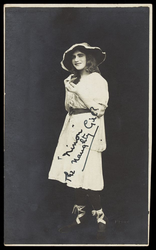 An amateur actor in drag, posing as 'Ninon', wearing a white dress and hat. Photographic postcard, 1929.