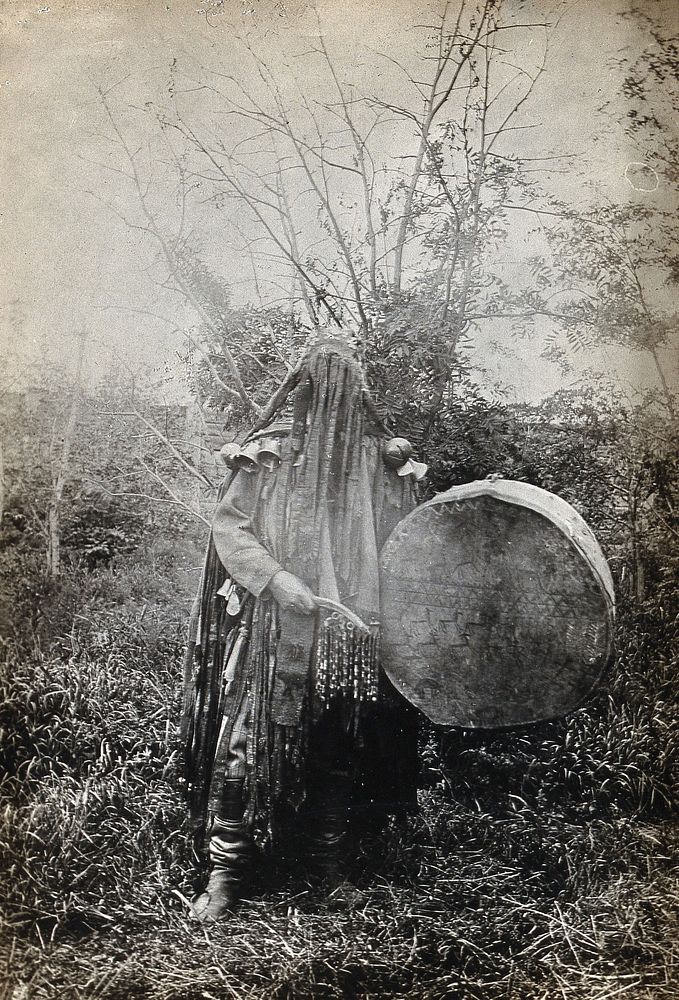 Minusinsk, Siberia: a Tartar medicine man or shaman in ceremonial dress with a covered face, holding a drum. Photograph, ca.…