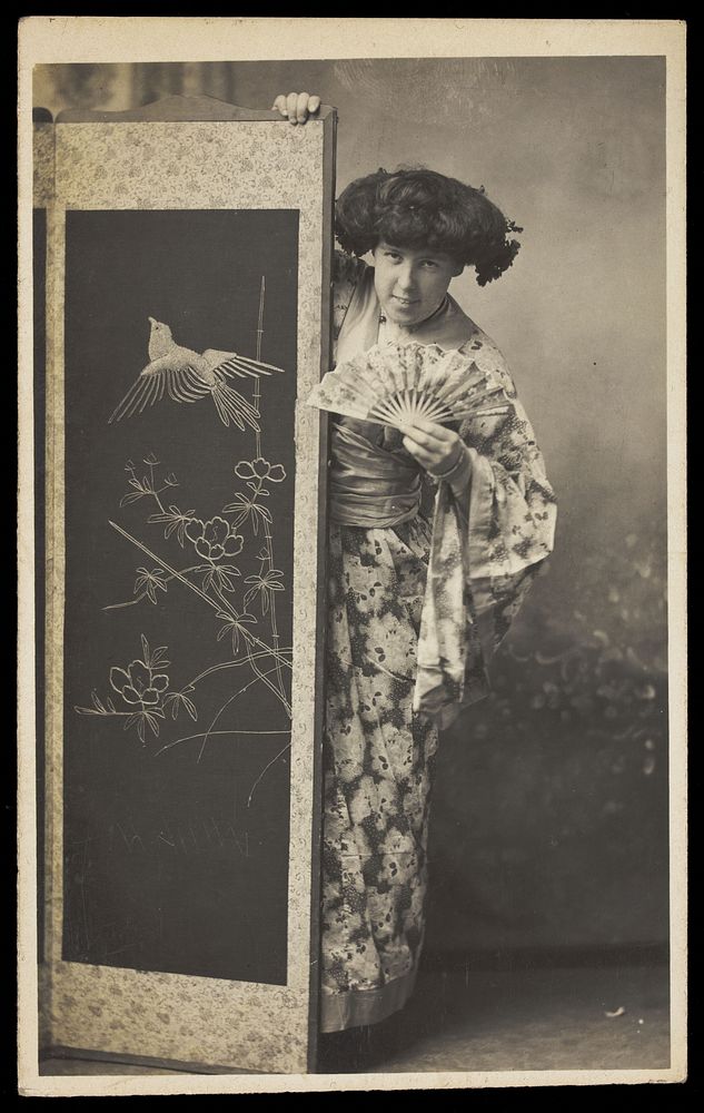 A man wearing a kimono posing from behind a screen.