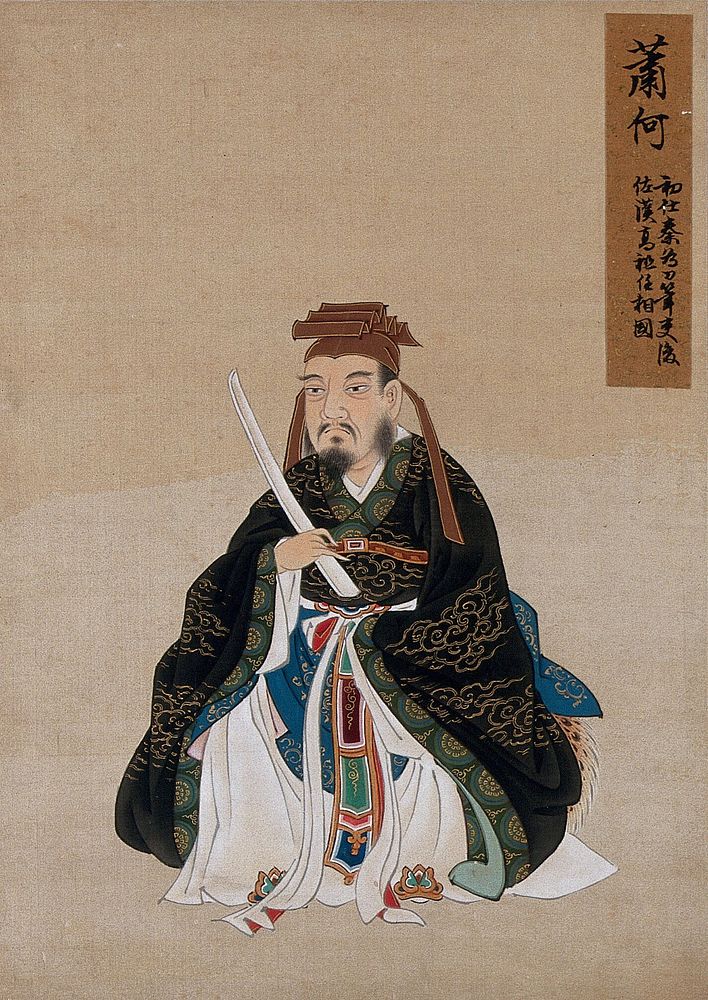 A Chinese figure wearing black silk robes with a green border, richly decorated with cloud scroll designs in gold thread.…