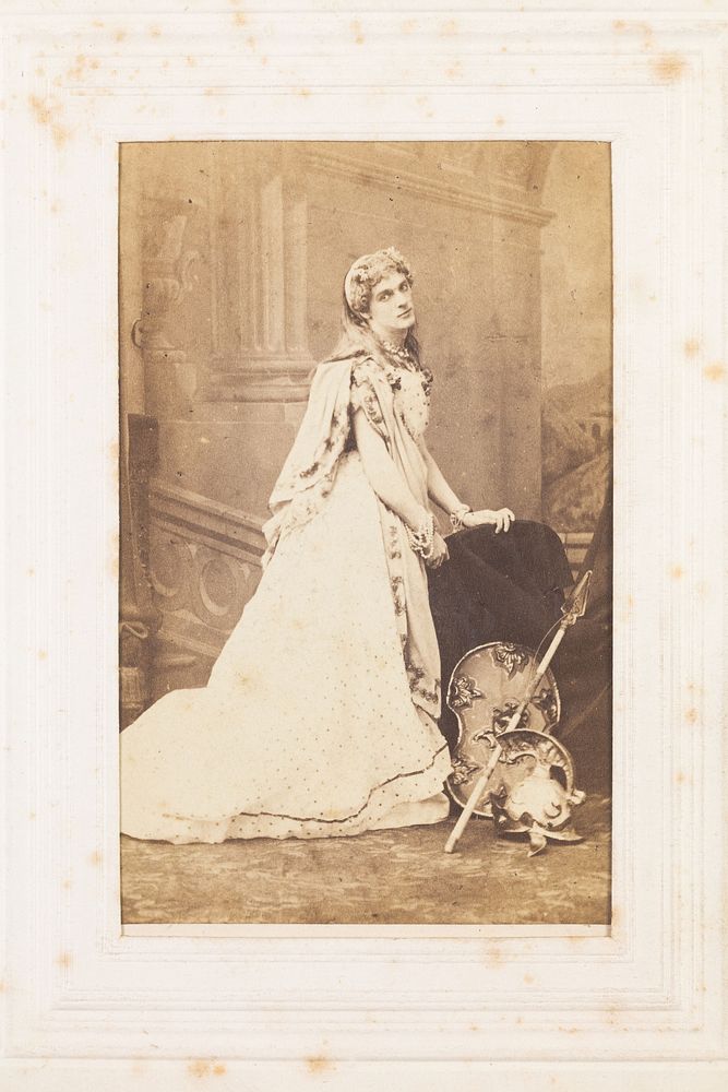 A man in drag posing in bridal costume next to Centurion-style props. Photograph, 189-.
