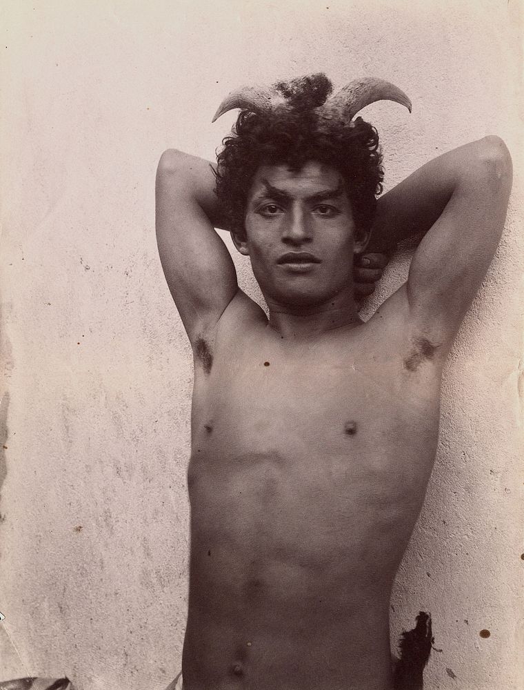 A Sicilian boy naked from the waist up, his hands behind his head, wearing horns.