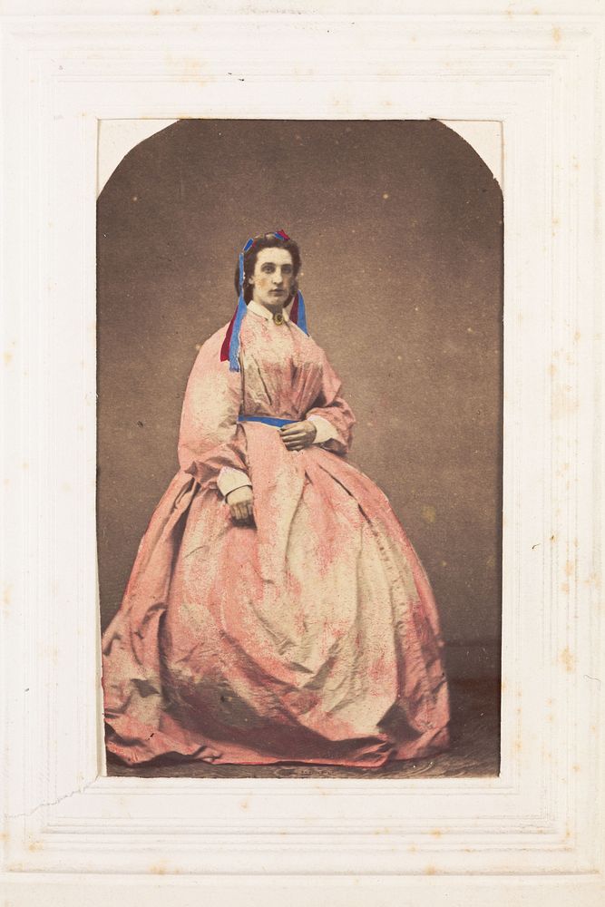 A man in drag poses wearing a large pink dress. Photograph, 189-.