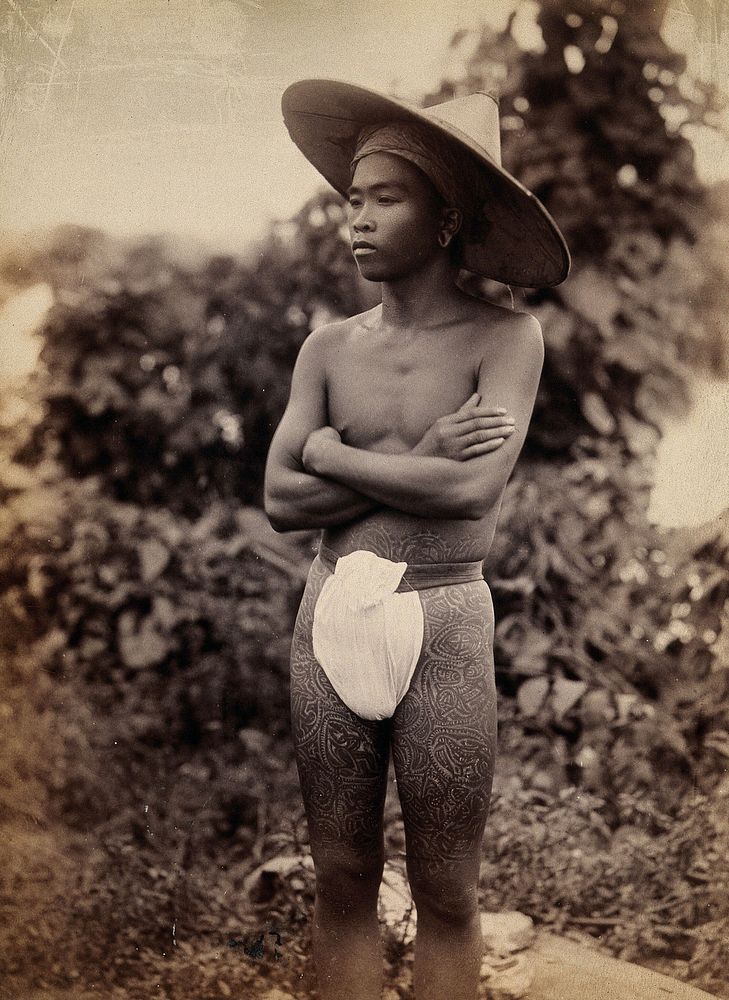 Myanmar (Burma): a young man with elaborate tattoos on his waist and thighs. Photograph.