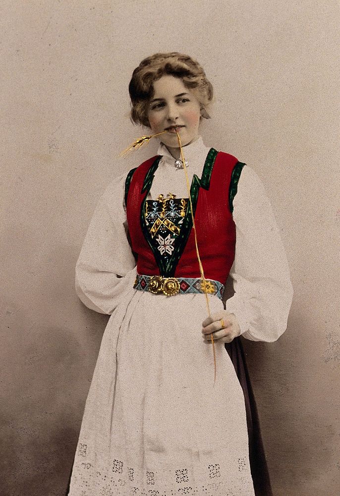 A young Norwegian woman, posing in a photographic studio wearing peasant dress. Coloured photograph by S. Lund, 1903.