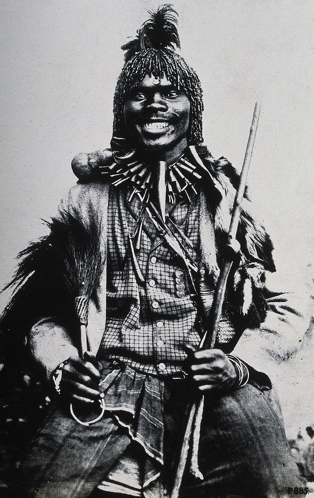 Africa: a medicine man in ceremonial dress holding a staff and a whisk. Reproduction of a photograph, 1880/1900 .