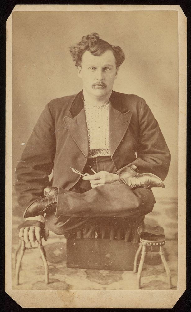 I.D. Waterman, seated, cross-legged, holding a carte de visite photograph. Photograph by C.W. Terpening, 1876.