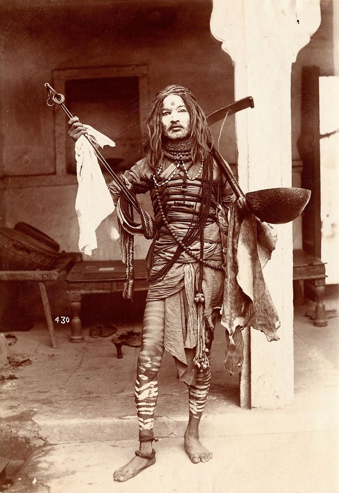 A young Indian man wearing many beads and makeup in a temple precinct. Photograph, ca.1900.