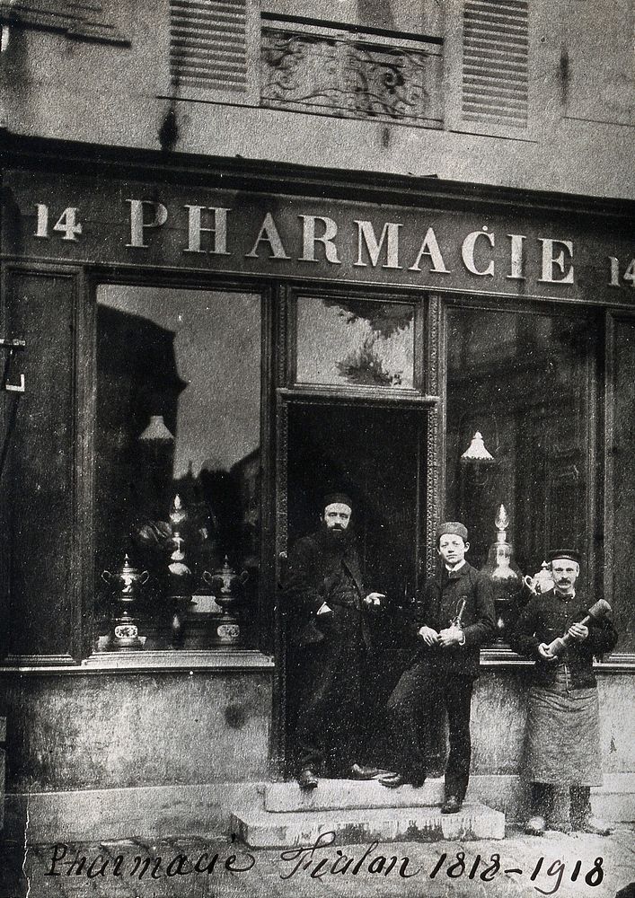 The Pharmacie Fialon in France: two men and a boy wearing hats, standing on the steps. Photograph.