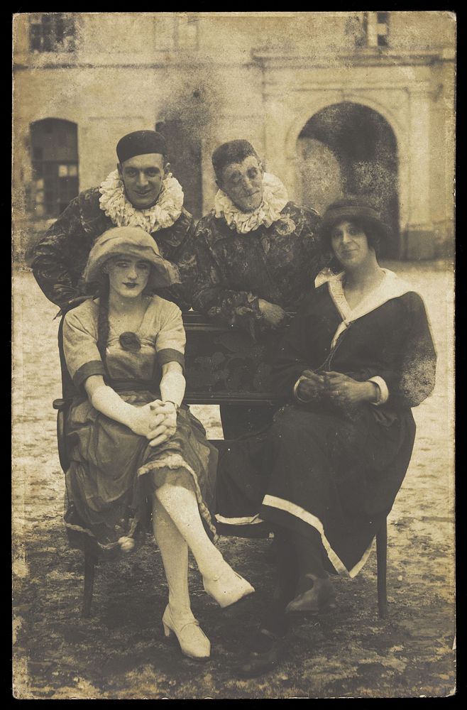 Members of 'The Stars' concert party, two soldiers in drag and two as pierrots, pose around a bench. Photographic postcard…