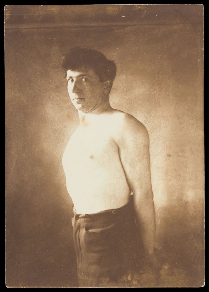 A man standing barechested with his arms behind his back. Photograph, 190-.