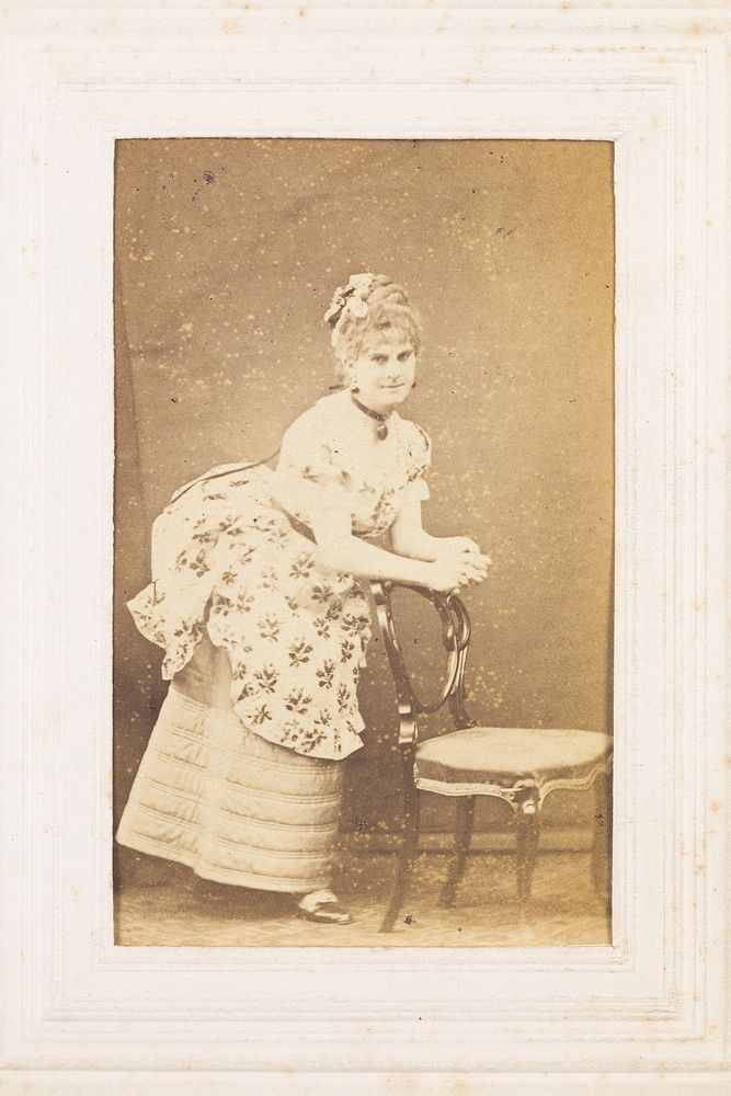 A man in drag resting against a chair. Photograph, 187-.