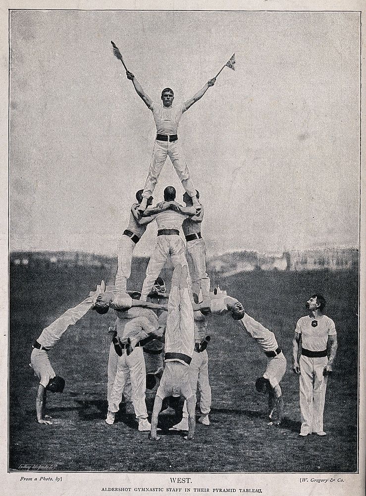 A number of men have formed a pyramid as part of a gymnastic exercise. Process print.