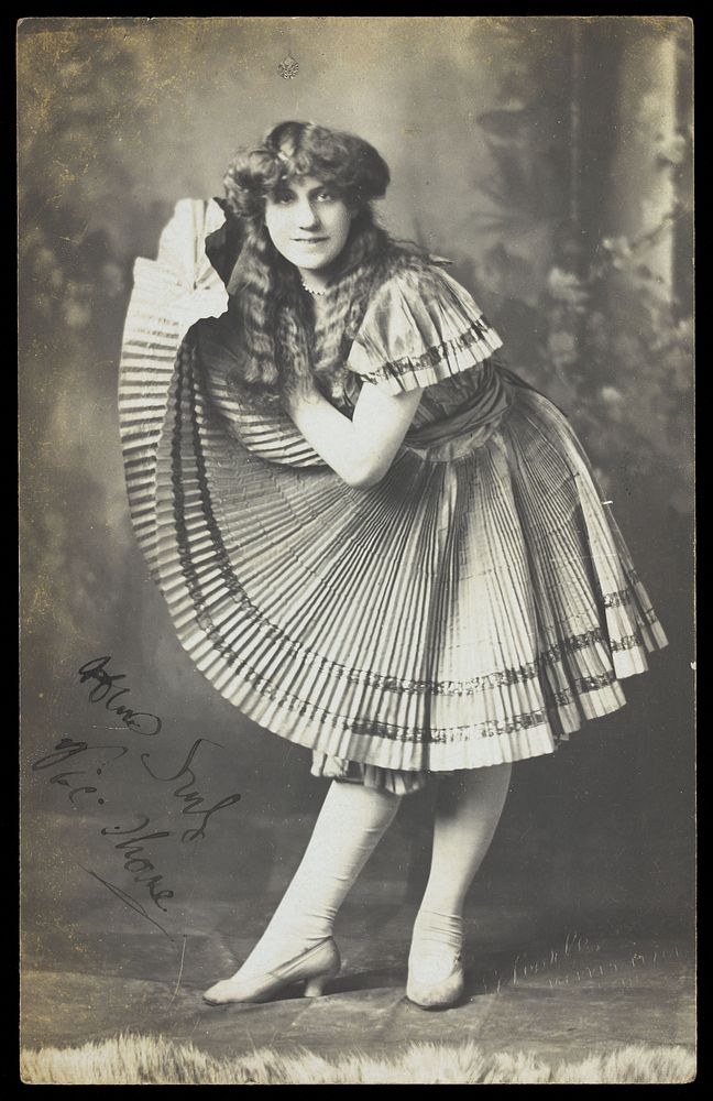 An amateur actor in drag holds up his impressive folded dress to one side. Photographic postcard, 191-.