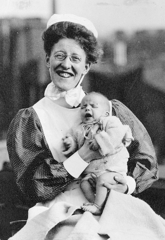 General Lying In Hospital, York Road, Lambeth: nurse sitting holding baby. Photograph, 1908.