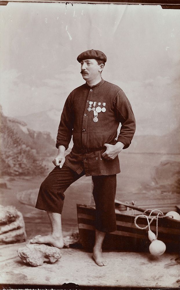 A barefoot Basque fisherman posing with several medals on his tunic.
