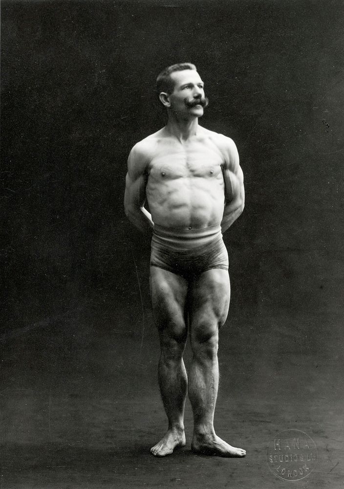 A male bodybuilder wearing bathing trunks, posing in a studio setting.