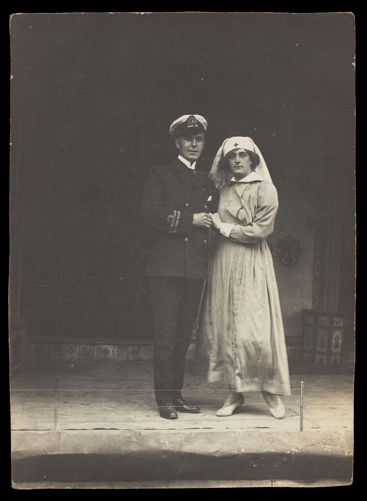 A couple of sailors, one in drag, pose together on stage. Photographic postcard, 191-.