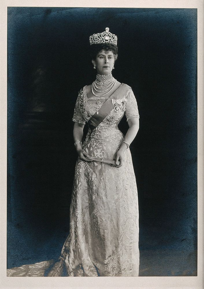 Queen Mary (May of Teck) standing, wearing a tiara and holding a folded fan. Photograph by John Thomson, ca. 1910.