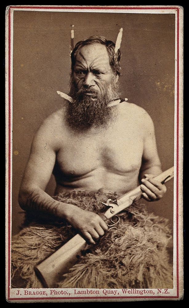 A Maori man with a tattoed face, holding a rifle. Photograph by J. Bragge, 188-.