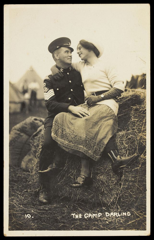 Two soldiers embracing on a bale of hay, one in drag. Photographic postcard, 191-.