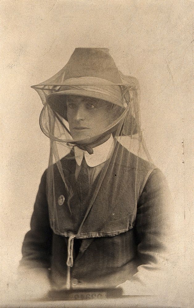 Mosquito headnet worn over a hat, modelled by a man wearing a collar, jacket and tie. Photograph, 1902/1918 .