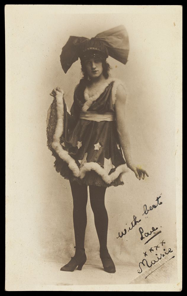 A man in drag poses wearing a short dress and large bow tie-shaped head garment. Photographic postcard, 192-.