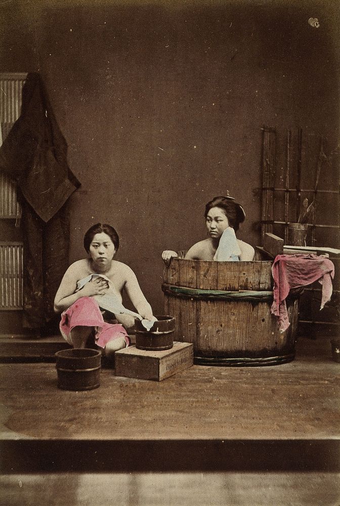 Japan: two women washing: one bathing in a wooden tub and one squatting down holding a flannel. Coloured photograph…