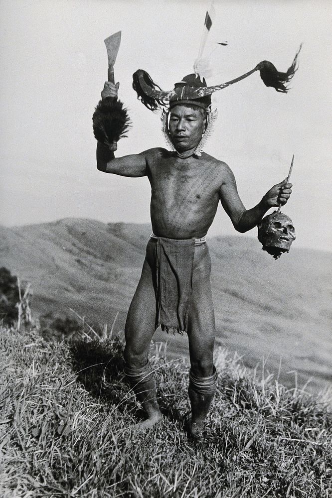 A young man of the Konyak Naga tribe, India, holding a human head. Photograph.