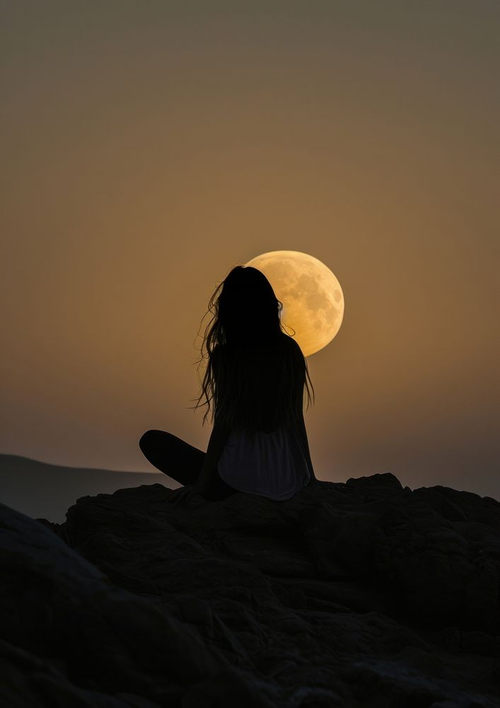A woman silhouette sitting put the hand together or doing yoga on the mountain in front of the moon backlighting astronomy…