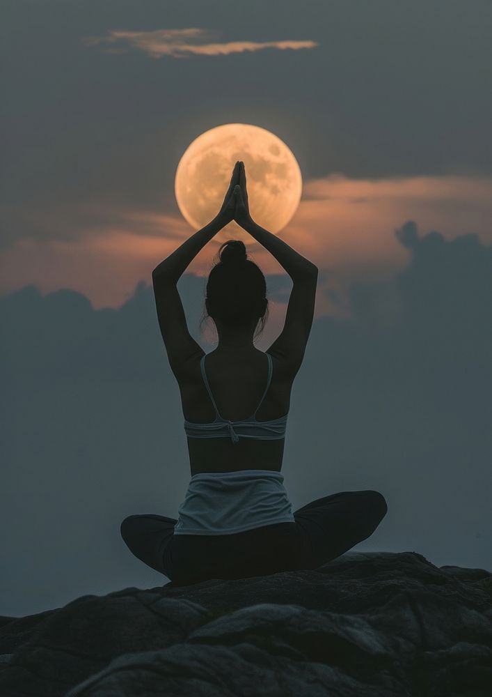 A woman silhouette sitting put the hand together above the head or doing yoga on the mountain in front of the moon astronomy…
