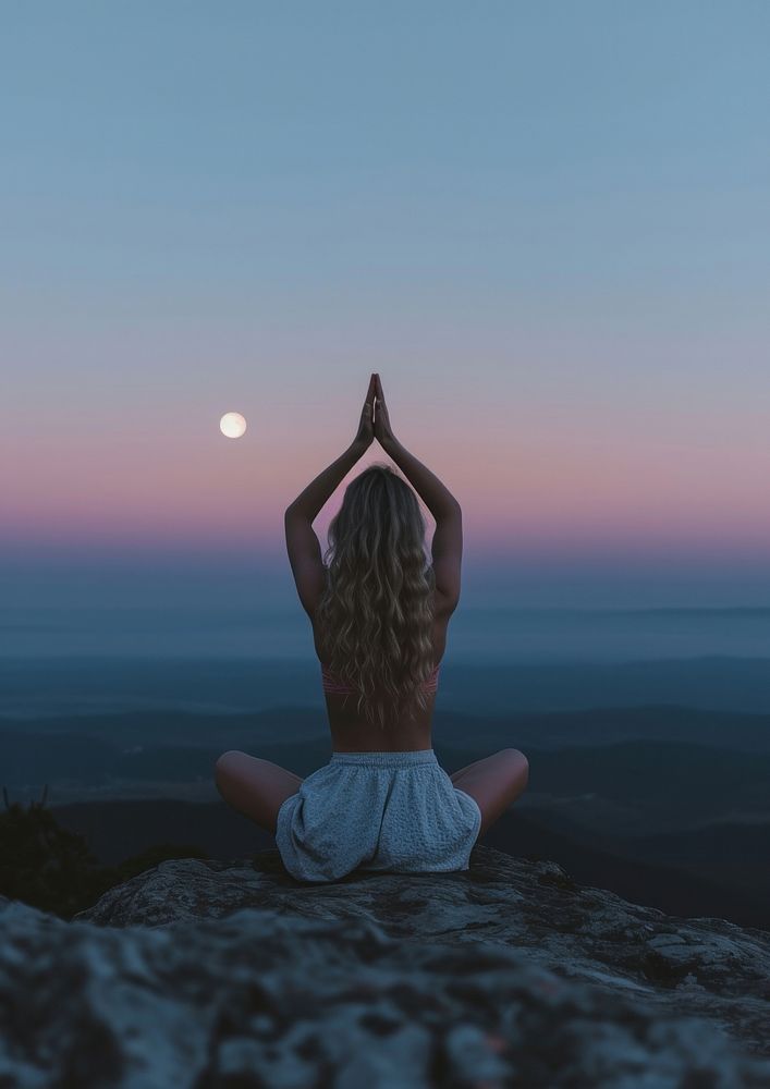 A woman silhouette sitting put the hand together above the head or doing yoga on the mountain in front of the moon astronomy…